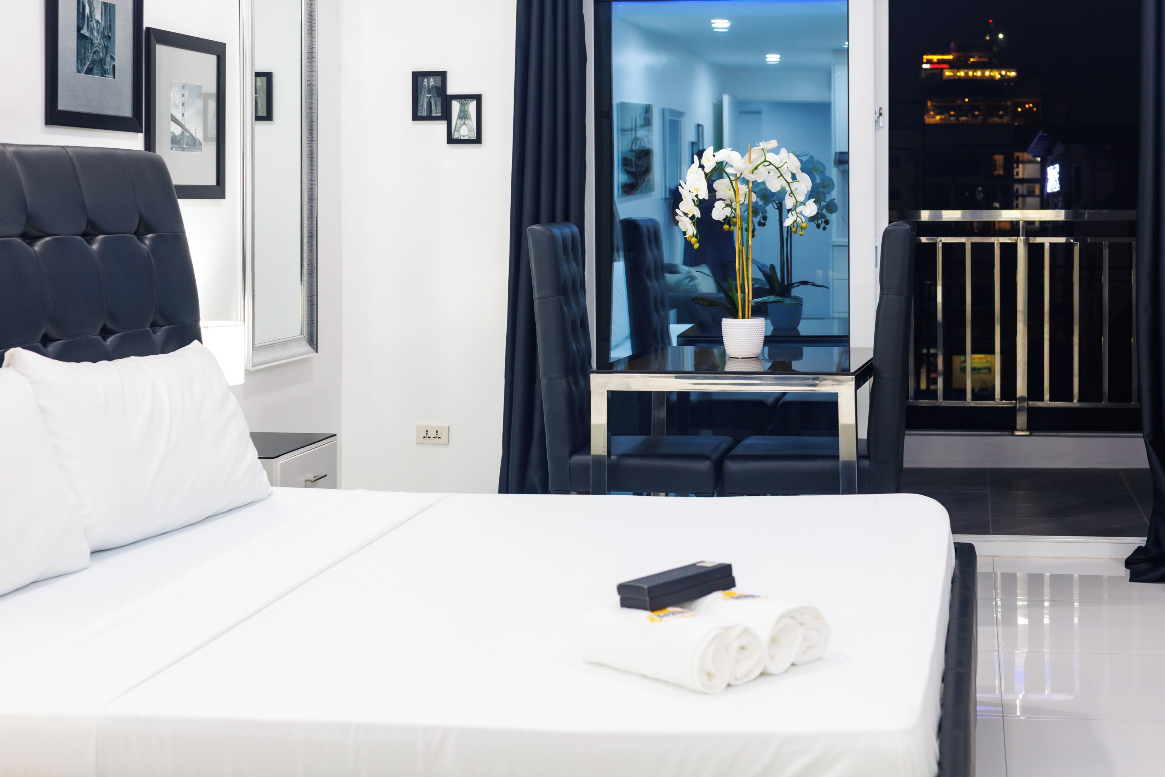 A hotel room with a bed, a desk with a potted plant, and a view of the cityscape.
