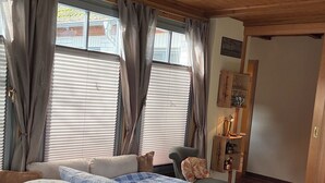 Quarto com cama, cortinas, uma cadeira, um armário de madeira e uma porta.