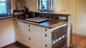 Uma cozinha com ilha central, vigas de madeira no teto e uma janela com cortinas.