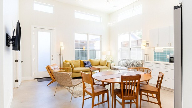 Uma sala de estar ampla com sofá, cadeiras, mesa de jantar e cozinha equipada com geladeira e armários.