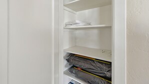 Ein weißer Kleiderschrank mit Regalen, auf einem befinden sich gefaltete weiße Handtücher und auf einem anderen verpackte Gegenstände.