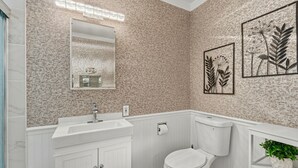Ein Badezimmer mit strukturierter Wand, einem weißen Waschbecken, einer Toilette und botanischen Bildern in Rahmen.