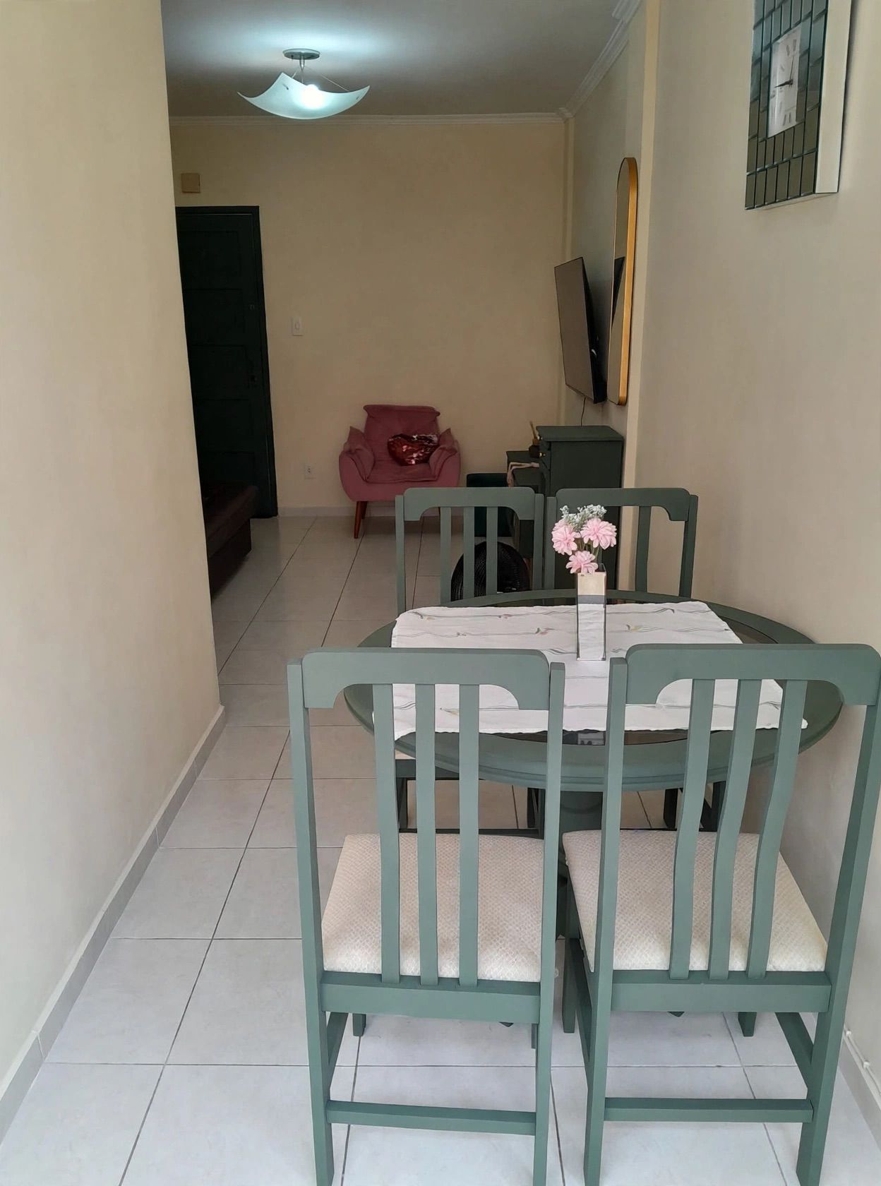 A dining area with a table set for four, green chairs, and a pink chair in the background.