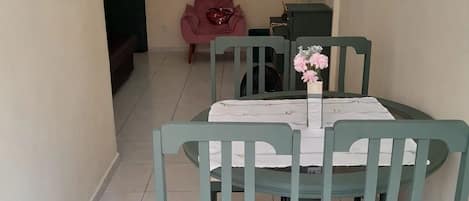 A dining area with a table set for four, green chairs, and a pink chair in the background.
