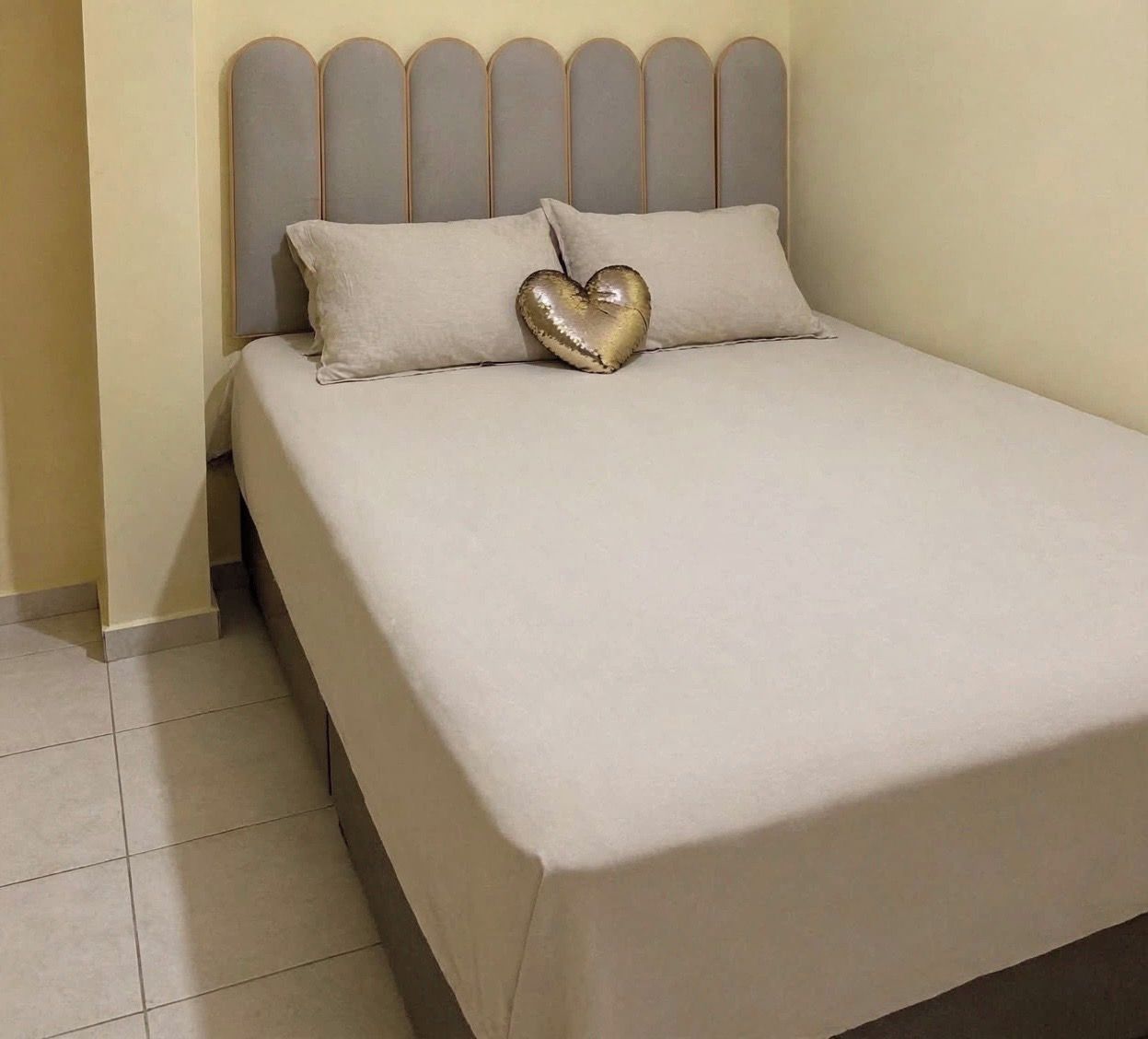 Ein Bett mit Kopfteil, einem herzförmigen Kissen und einer schlichten Wand.
