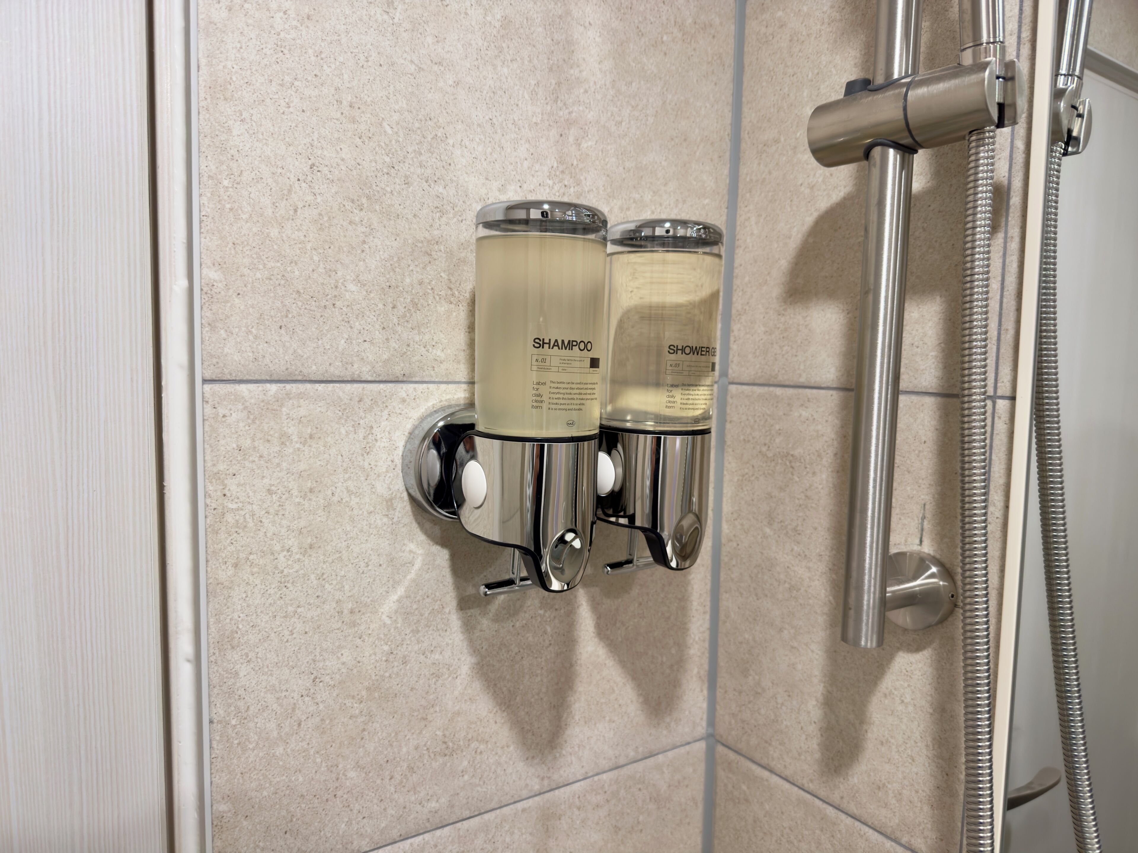 A shower area with a handheld showerhead and two shampoo bottles mounted on a wall.
