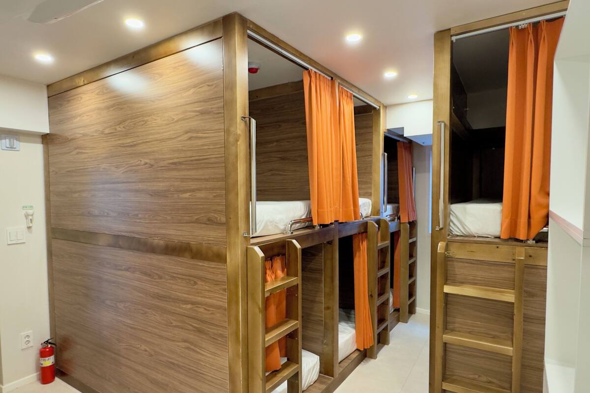 A room with bunk beds, wooden paneling, orange curtains, and a fire extinguisher.