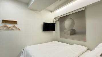 A hotel room with a bed, a mounted TV, a wooden hanger board, and a framed artwork on the wall.