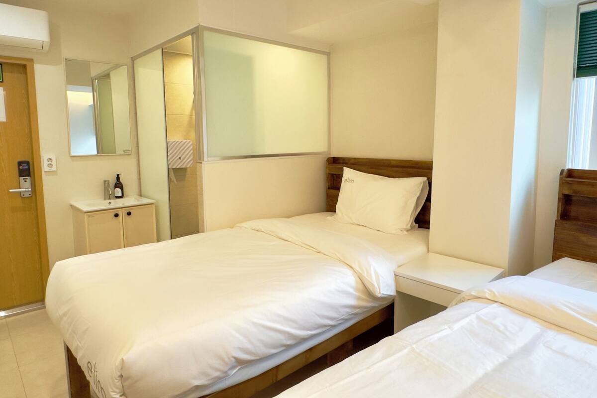 A hotel room with two beds, a bedside table, a mirror, and a small cabinet.