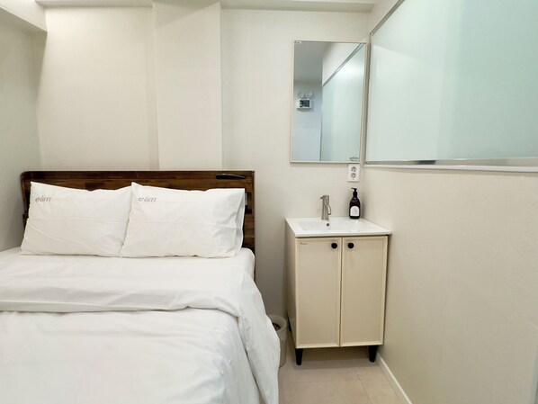 Una habitación de hotel con una cama, una mesita de noche con espejo y un armario pequeño.