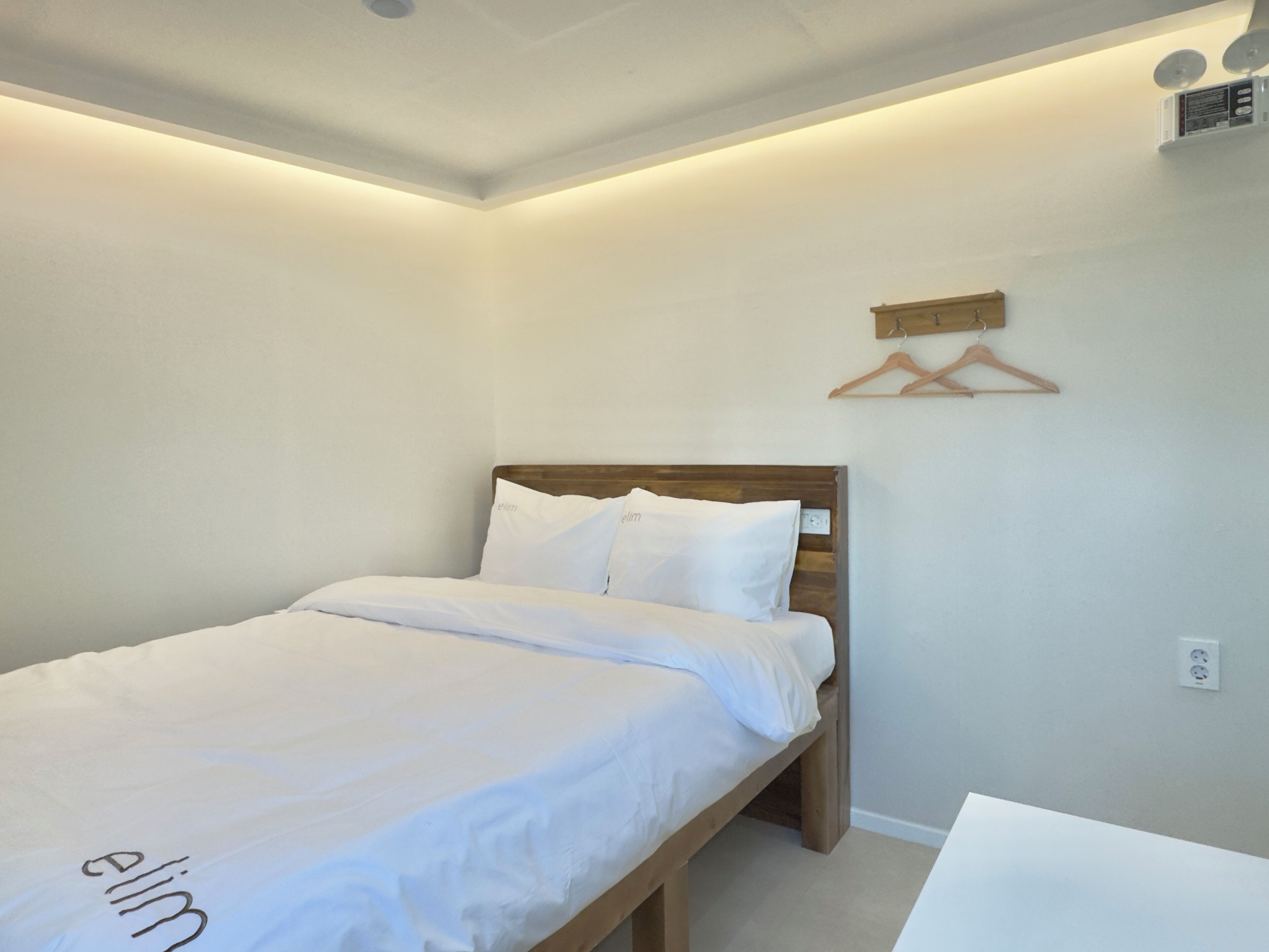 A single bed with a wooden headboard in a room with white walls and a ceiling light fixture.
