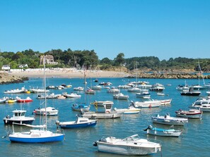 A marina with numerous boats docked, a sandy beach, and a forested hill in the background. - Ty Stef by Interhome (Nevez)
