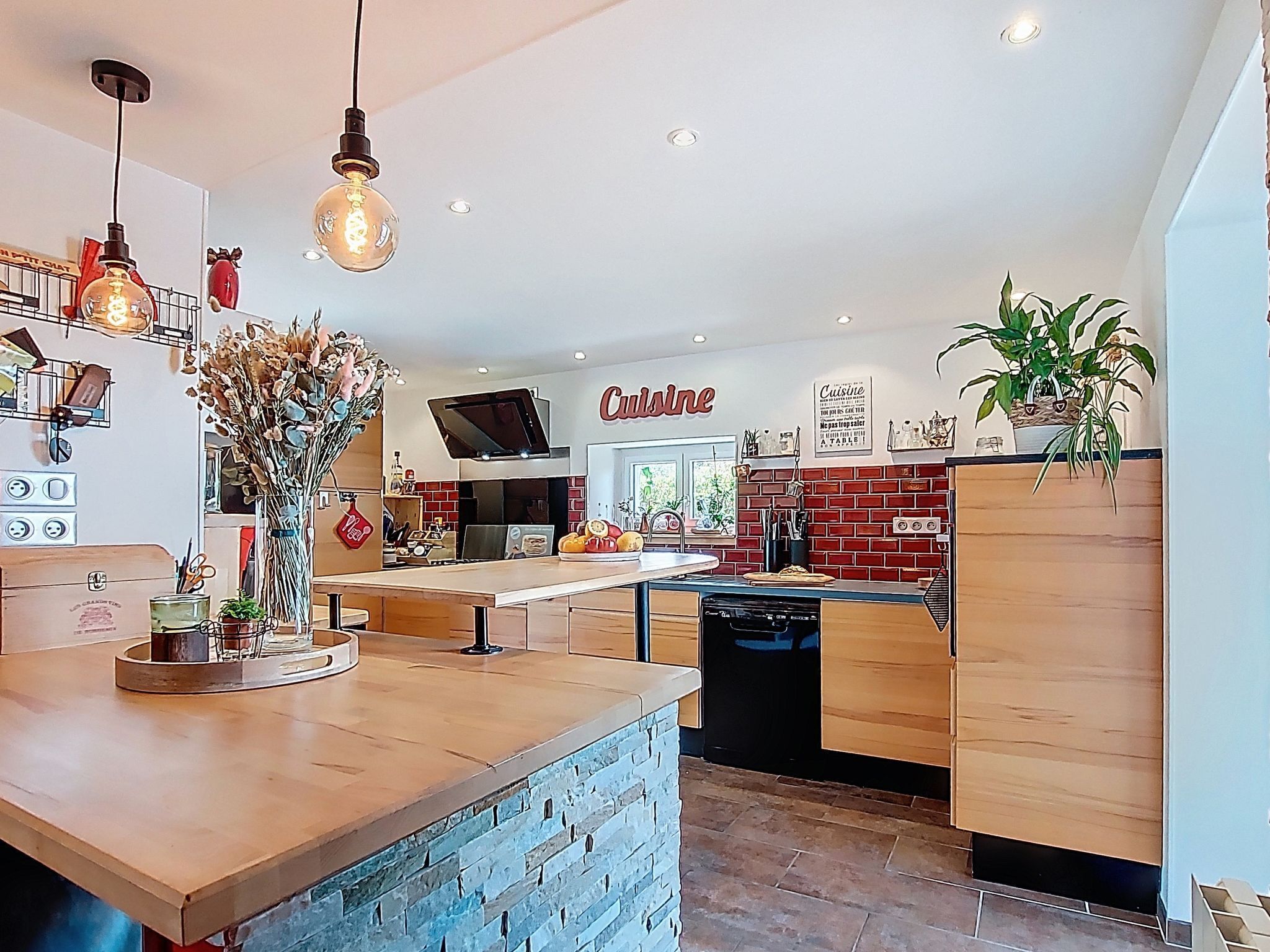 A modern kitchen with a central island, hanging pendant lights, and a brick accent wall.
