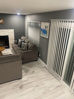 A living room with a grey sofa, patterned cushions, a fireplace, and a window with blinds. - Wonderful 3-bedroom house with AC in sunny Phoenix (Phoenix)