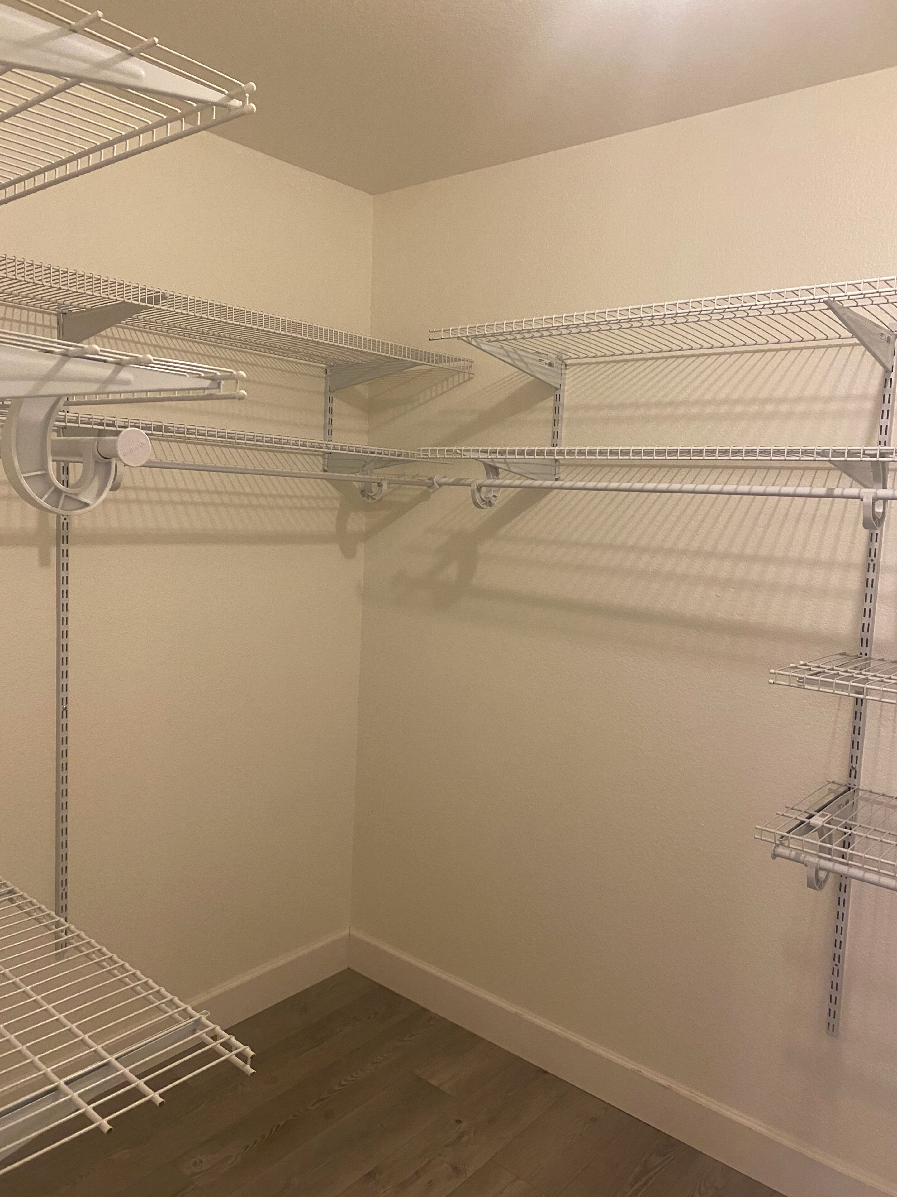 A corner closet with metal shelving units, a wooden floor, and a white wall.