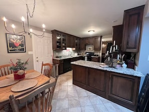Une cuisine avec des meubles en bois foncé, un plan de travail en granit, une table à manger avec des chaises et un lustre.