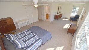 Ein Schlafzimmer mit Bett, Schreibtisch, Stuhl, Kleiderschrank und einem durchgehenden Türrahmen sichtbaren Badezimmer.