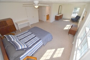 Ein Schlafzimmer mit Bett, Schreibtisch, Stuhl, Kleiderschrank und einem durchgehenden Türrahmen sichtbaren Badezimmer.