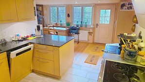 A kitchen with wooden cabinets, a central island, a stove, and a dining area with a table and chairs. - Rüttimätteli by Interhome (Marbach)