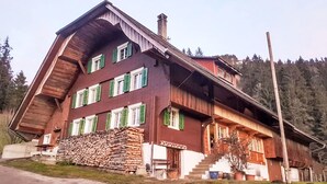 A multi-story wooden building with a sloped roof, a stack of firewood, and a staircase leading to the entrance. - Rüttimätteli by Interhome (Marbach)