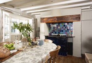 Een eetgedeelte met een tafel voor vier personen, een vaas met bloemen en een keuken met een kleurrijke tegelachtergrond.