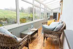 Ein Wintergarten mit Korbmöbeln, einem Tisch mit Gläsern und Blick ins Freie.