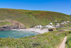 A coastal village with houses on a hillside, a sandy beach, and a clear blue sky. - Little Penrose Cottage is a spacious and characterful home set in mature gardens (Bude)