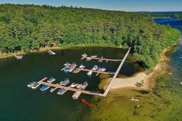 Luftaufnahme eines Yachthafens mit vertäuten Booten, umgeben von dichtem Wald und blauem Himmel.