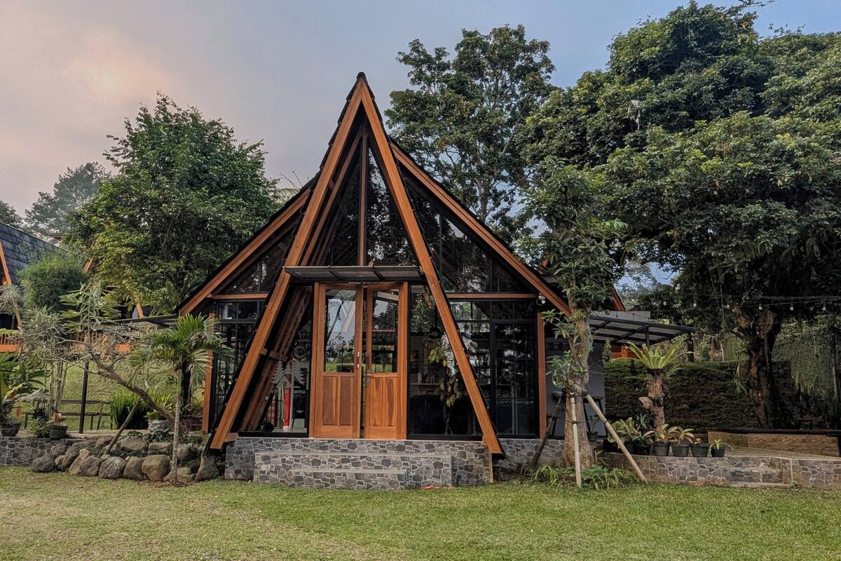 A triangular wooden structure with a glass door, surrounded by a stone wall and lush greenery.