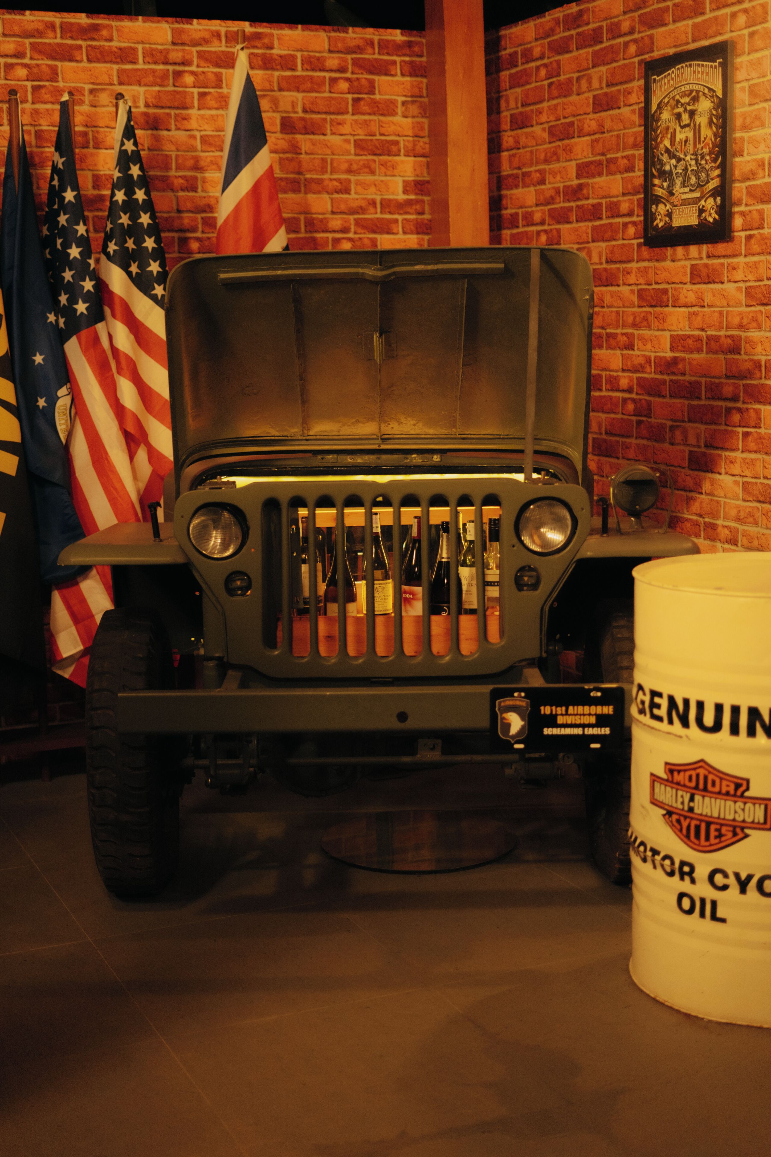 A vintage military jeep, flags, and a Harley-Davidson oil barrel.