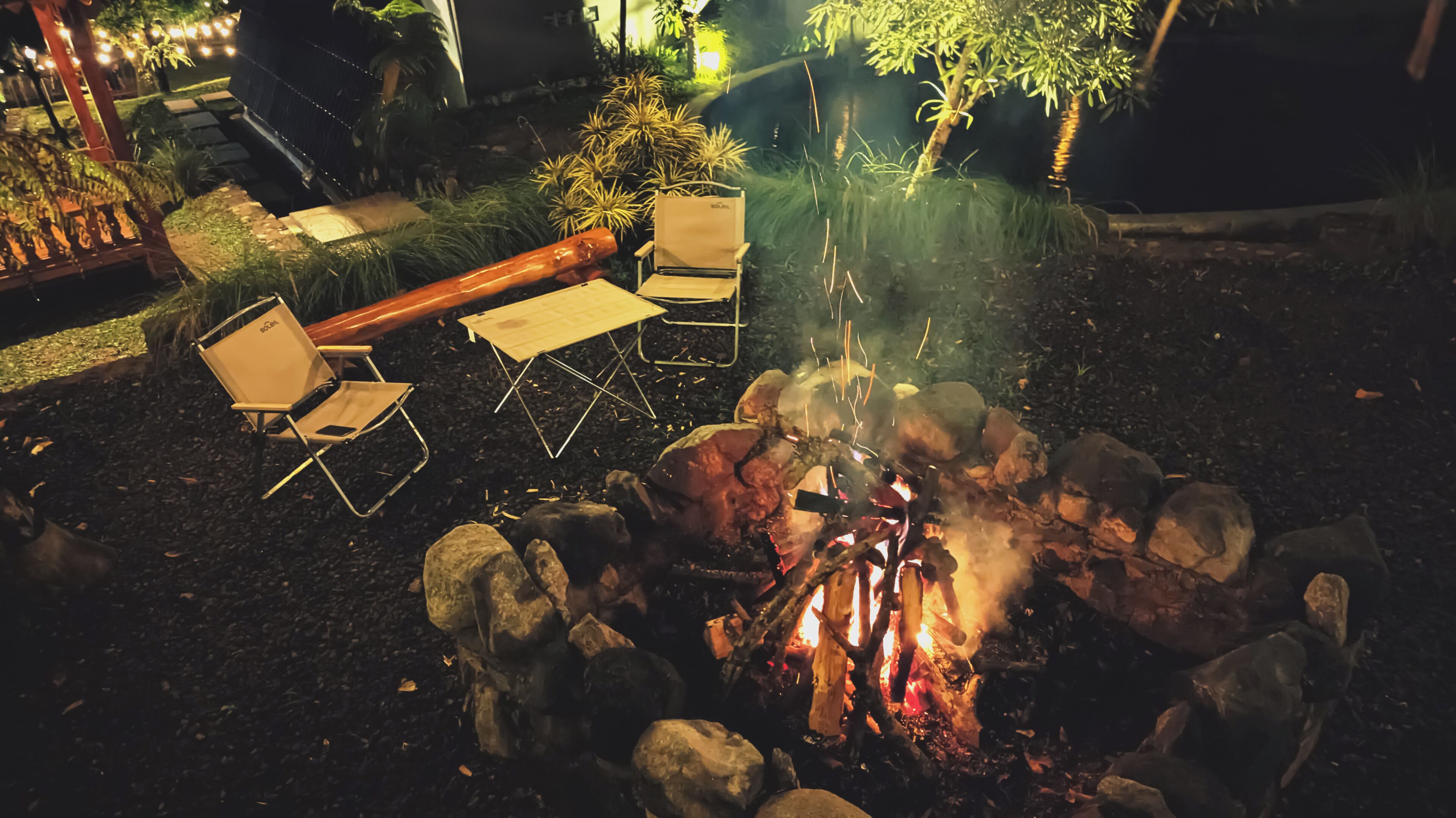 Ein Lagerfeuer mit Steinen, zwei Klappstühlen und einem Tisch.
