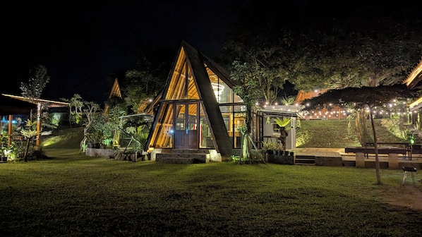 A triangular-shaped building with a glass facade, surrounded by a well-lit garden and outdoor seating area.