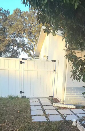 A gated backyard with a stone pathway, a white fence, and a brick wall. - Cozy bedroom with a little kitchen (Spring Hill)