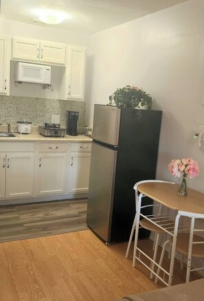 A compact kitchen with white cabinets, a stainless steel refrigerator, a microwave, and a small dining table with chairs. - Cozy bedroom with a little kitchen (Spring Hill)