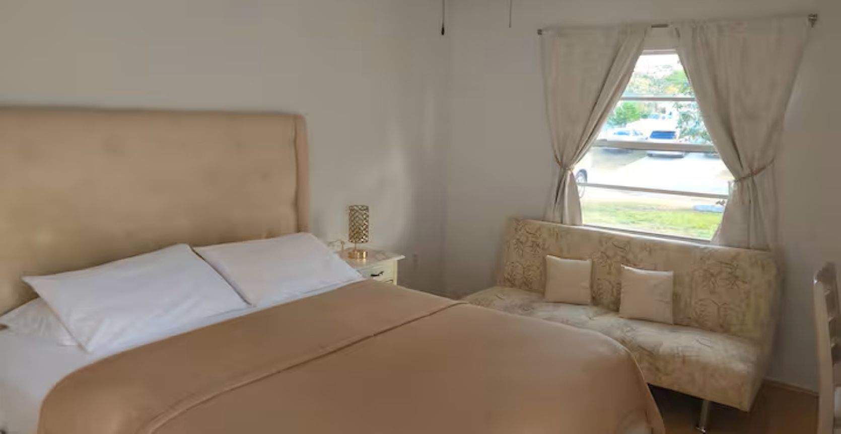 Une chambre à coucher avec un lit, un canapé, une table de chevet et une fenêtre avec des rideaux.
