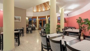 A restaurant with round tables and chairs, a high ceiling with a skylight, and a view of the street outside. - Hotel Millennium (Pecs)