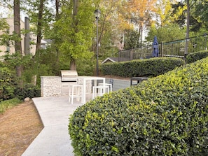 A patio area with a grill, white outdoor furniture, and a stone wall.