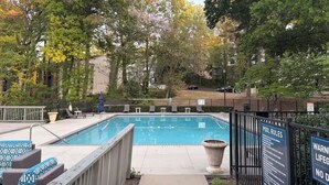 A swimming pool with lounge chairs, a wooden deck, and a fenced area with a signboard. - Lovely stay by the Braves / 2bd 2bth with private access gate to Braves Stadium (Smyrna)