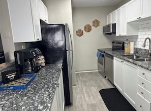 A kitchen with white cabinets, a black refrigerator, a coffee maker, and a microwave.