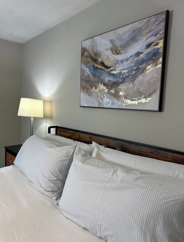 A hotel room with a bed, a nightstand, a lamp, and a wall-mounted abstract painting.