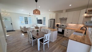 A modern kitchen with white cabinets, a wooden dining table, and a built-in oven. - Brand New 2026 Country Cottage ! (Wiarton)