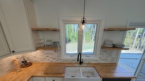 Eine moderne Küche mit weißen Schränken, einer Holzarbeitsplatte, einer integrierten Spüle und einem Fenster mit Blick auf Grünflächen.