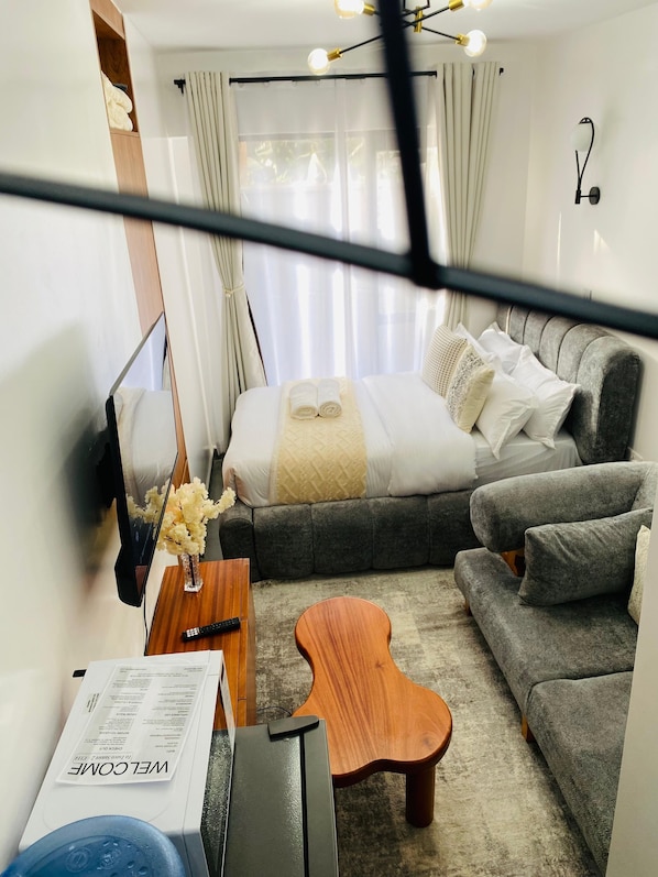 A hotel room with a bed, sofa, coffee table, TV, and a welcome brochure.