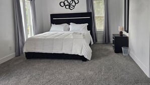 Een slaapkamer met een groot bed, een hoofdbord, een nachtkastje met een lamp en een wanddecoratie.