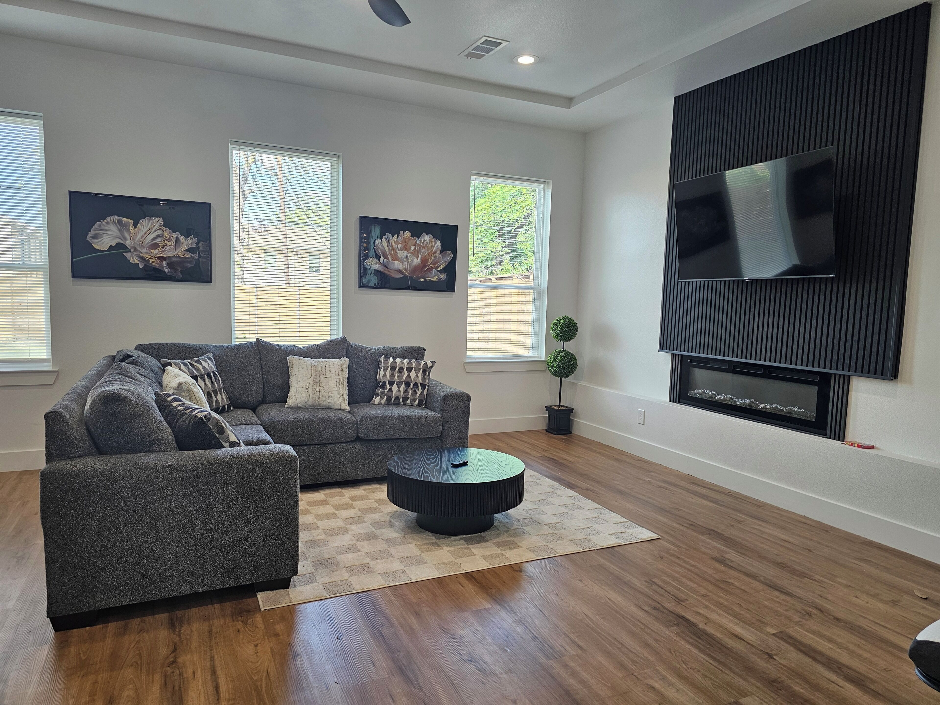A living room with a grey sectional sofa, two wall-mounted TVs, and a potted plant.