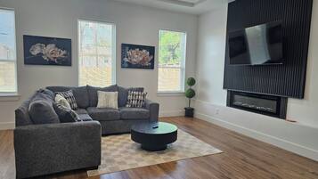 A living room with a grey sectional sofa, two wall-mounted TVs, and a potted plant.