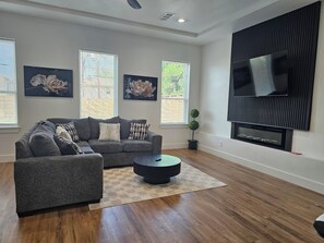 Ein Wohnzimmer mit einem grauen Ecksofa, zwei Wand-Fernsehern und einer Topfpflanze.