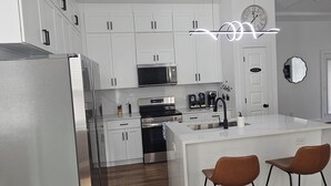 Een moderne keuken met witte kasten, roestvrijstalen apparatuur, een centraal eiland met barstoelen en een wandklok.