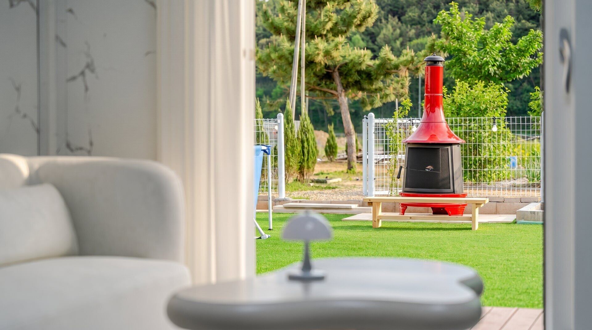 A modern living room with a view of a red outdoor heater and a fenced garden area.