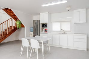 Una cocina moderna con armarios blancos, un refrigerador de acero inoxidable y una escalera de madera.